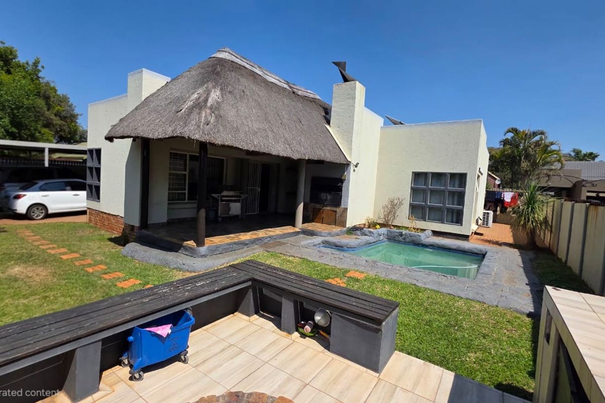 Rear exterior view featuring a thatched roof patio, built-in braai area, and a small swimming pool set within a private garden.