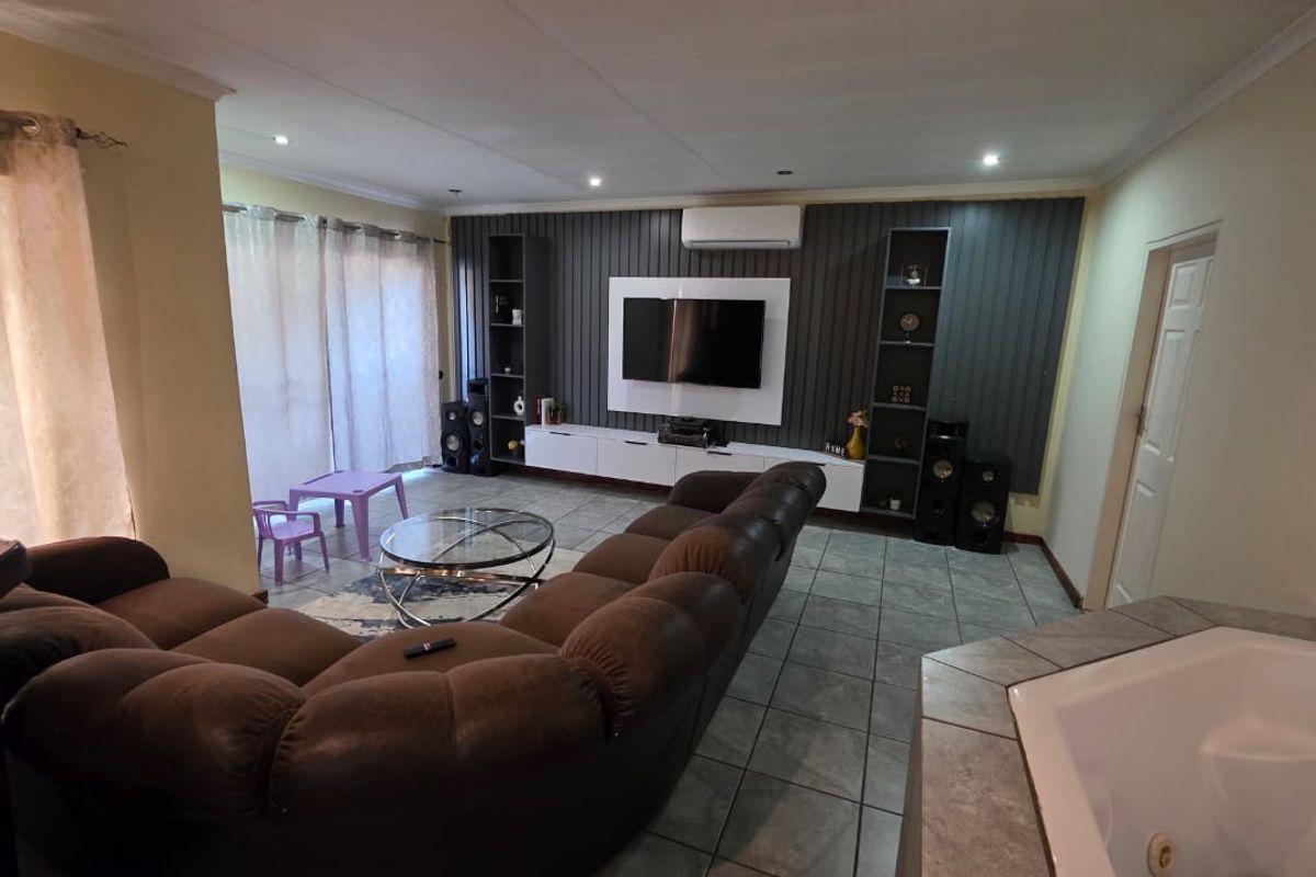 Spacious living room featuring a modern built-in media wall, tiled flooring, air conditioning, and sliding glass doors leading to an outdoor area.