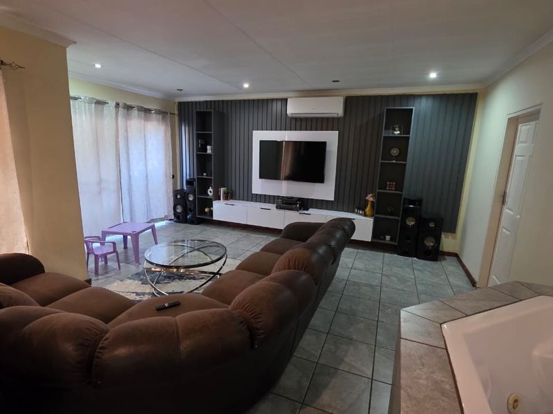 Spacious living room featuring a modern built-in media wall, tiled flooring, air conditioning, and sliding glass doors leading to an outdoor area.