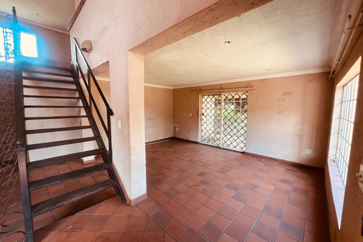 An empty, open-plan living area featuring terracotta tiled flooring, a wooden staircase, and a sliding door leading to the exterior.