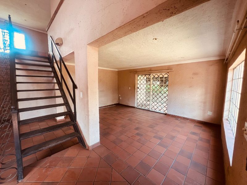 An empty, open-plan living area featuring terracotta tiled flooring, a wooden staircase, and a sliding door leading to the exterior.