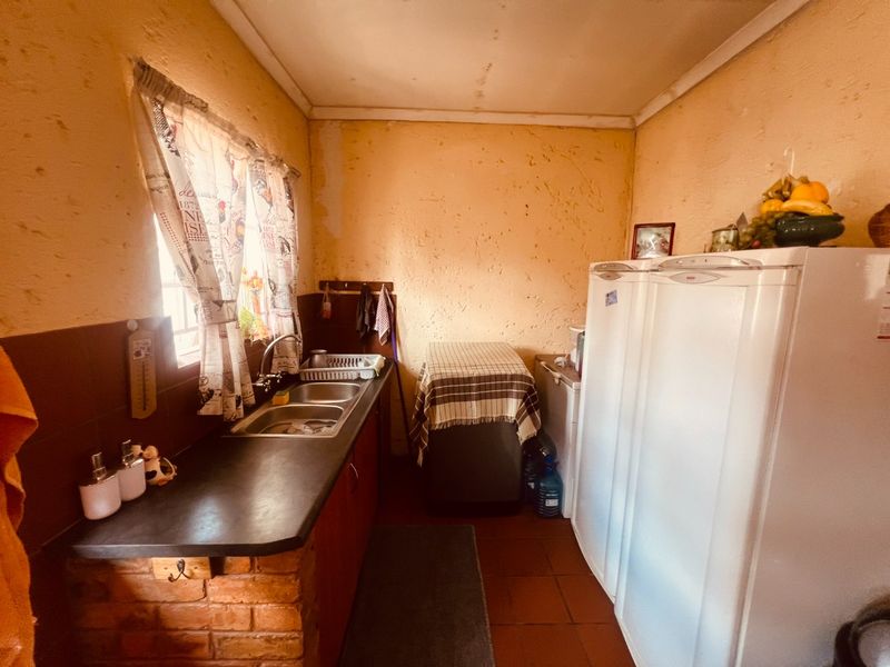 A functional scullery area featuring a double basin sink, brick-based cabinetry, and tiled splashbacks, currently requiring cosmetic wall repairs and updates.