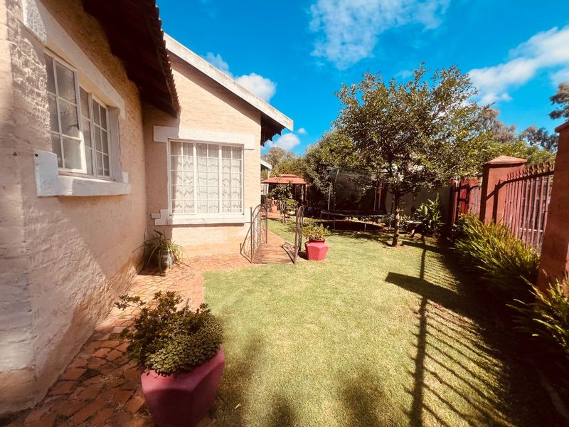 A view of the rear garden featuring a lawn, brick paved pathway, and perimeter fencing alongside the plastered exterior of the house.