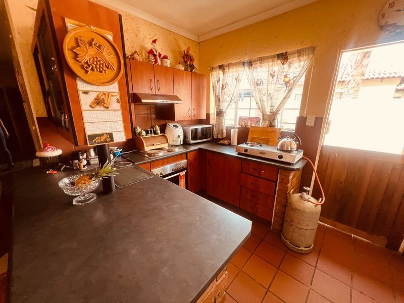 A functional kitchen featuring built-in wooden cabinetry, tiled flooring, and a gas hob setup with direct access to the exterior.