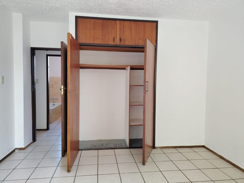 A bedroom featuring tiled flooring and a built-in wardrobe with overhead storage, providing direct access to an adjacent bathroom.