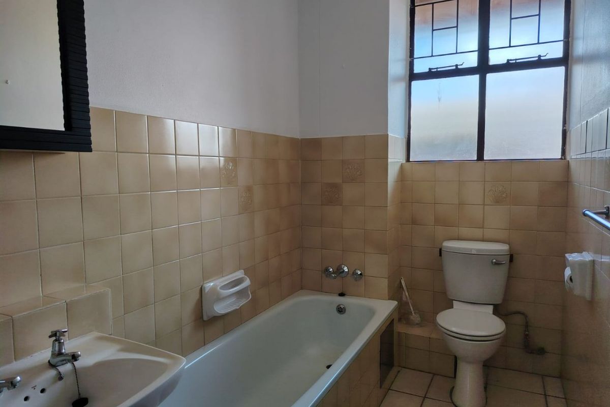 A dated bathroom featuring a standard bathtub, pedestal basin, and toilet with original wall and floor tiling.