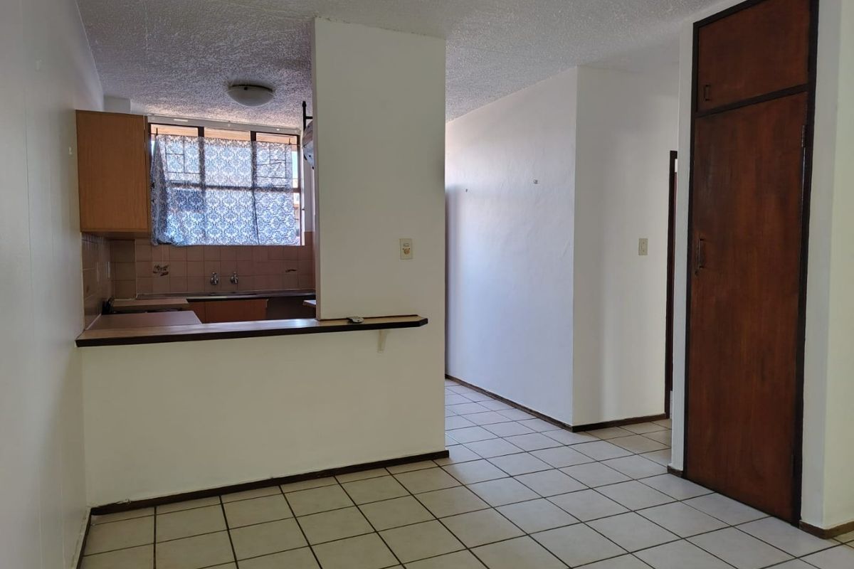 An open-plan living and kitchen area featuring tiled flooring, built-in cabinetry, and a breakfast counter, offering a blank canvas for renovation.