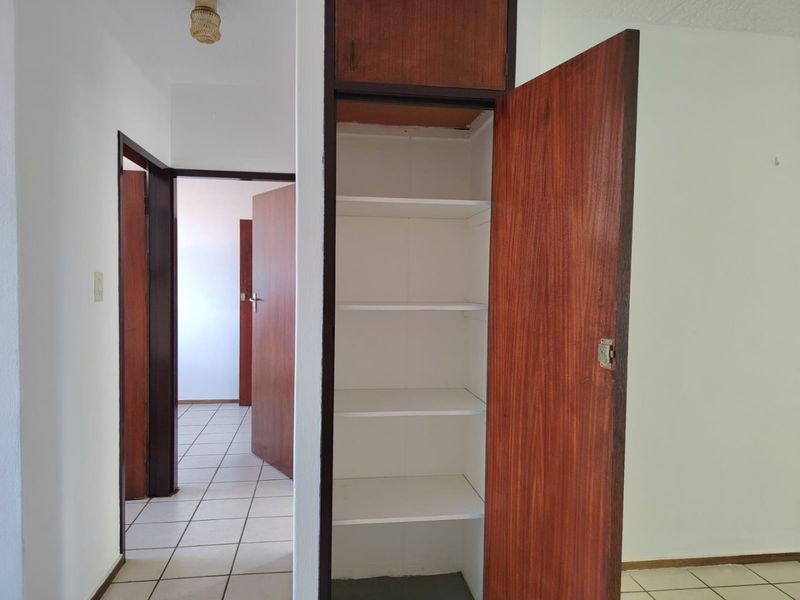 A functional hallway featuring tiled flooring and a built-in storage cupboard with wooden doors, providing access to adjacent rooms.
