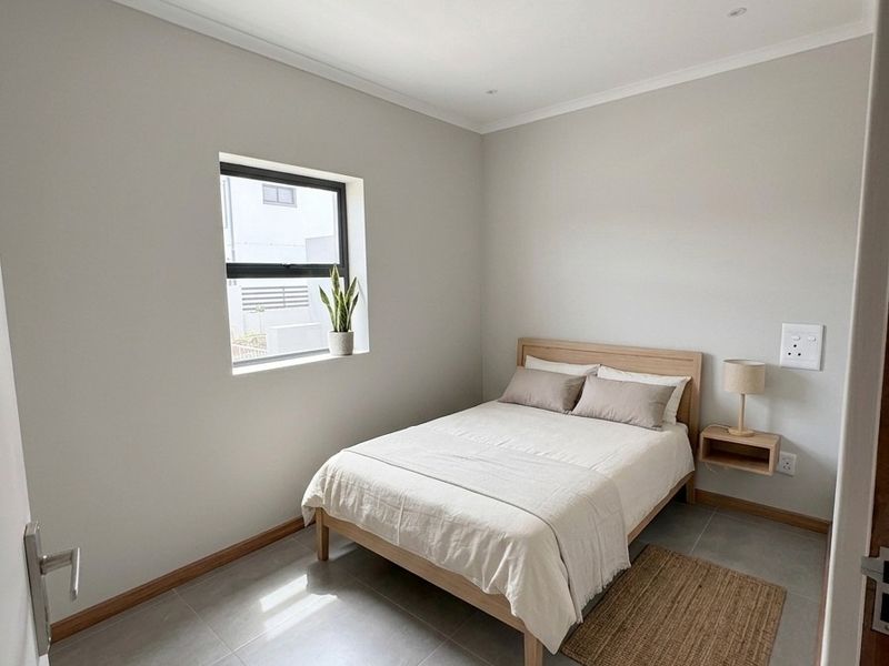 A clean, modern bedroom featuring neutral wall tones, large format floor tiles, recessed lighting, and an aluminium-framed window.
