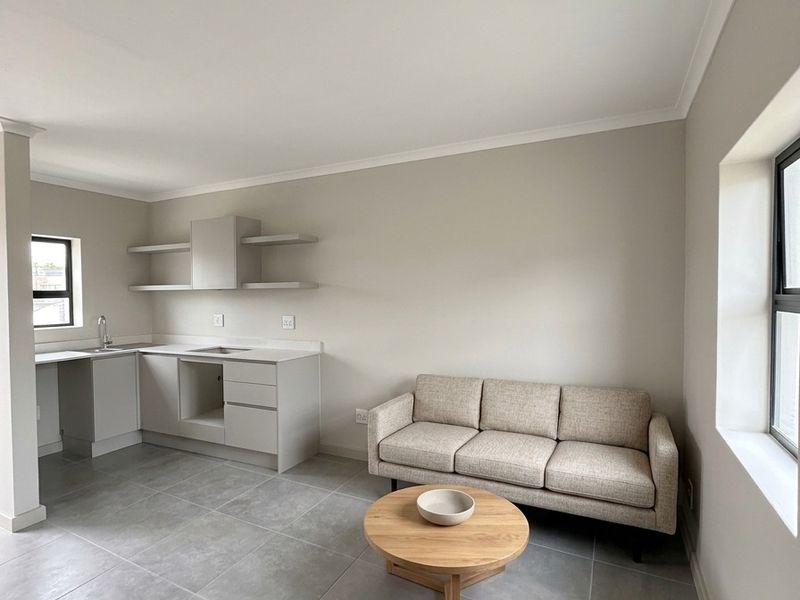 Modern open-plan living area featuring a compact kitchen with sleek cabinetry, floating shelves, extractor fan, and neutral tiled flooring throughout.