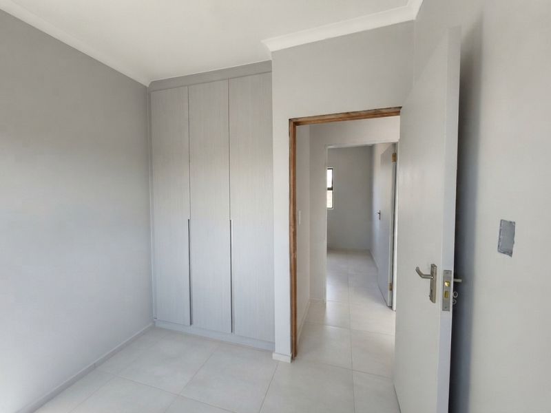 A clean, empty bedroom featuring modern built-in cupboards, neutral tiled flooring, and a neutral color palette, ready for personalization.