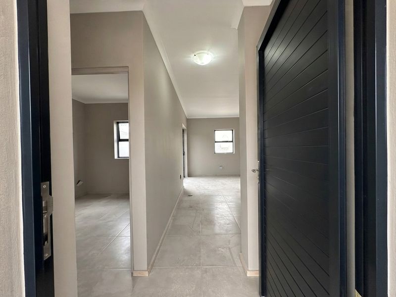 A clean, neutral-toned hallway featuring tiled flooring and modern internal doors, leading into adjacent empty living spaces.
