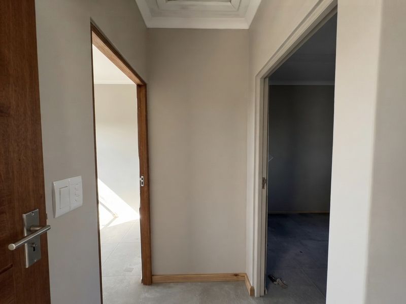 A neutral-toned hallway featuring timber door frames and coved ceiling cornicing, leading into two vacant rooms with tiled flooring.