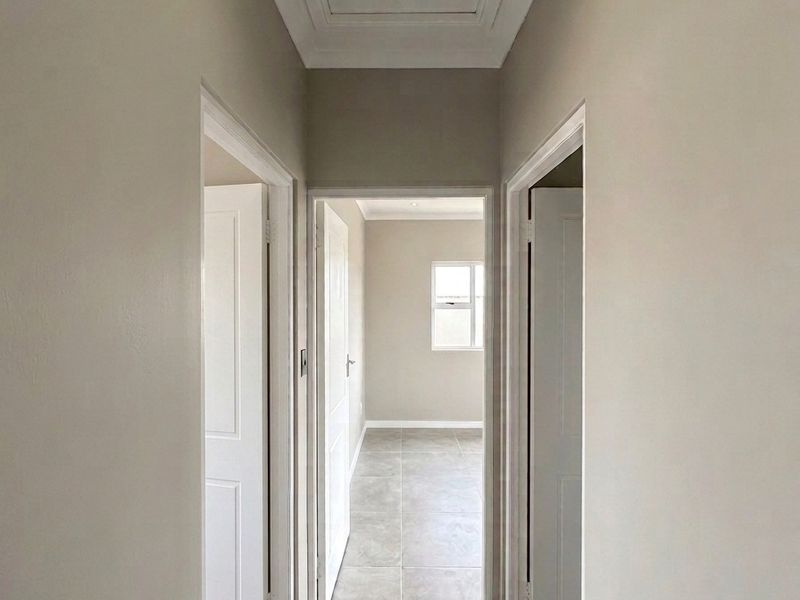 A clean, neutral-toned hallway featuring tiled flooring, recessed lighting, and a loft access hatch, leading into adjacent rooms.