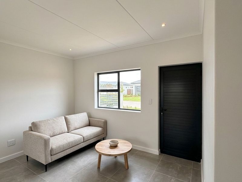 A bright, modern living area featuring neutral tiled flooring, recessed lighting, and a contrasting black door and window frame.