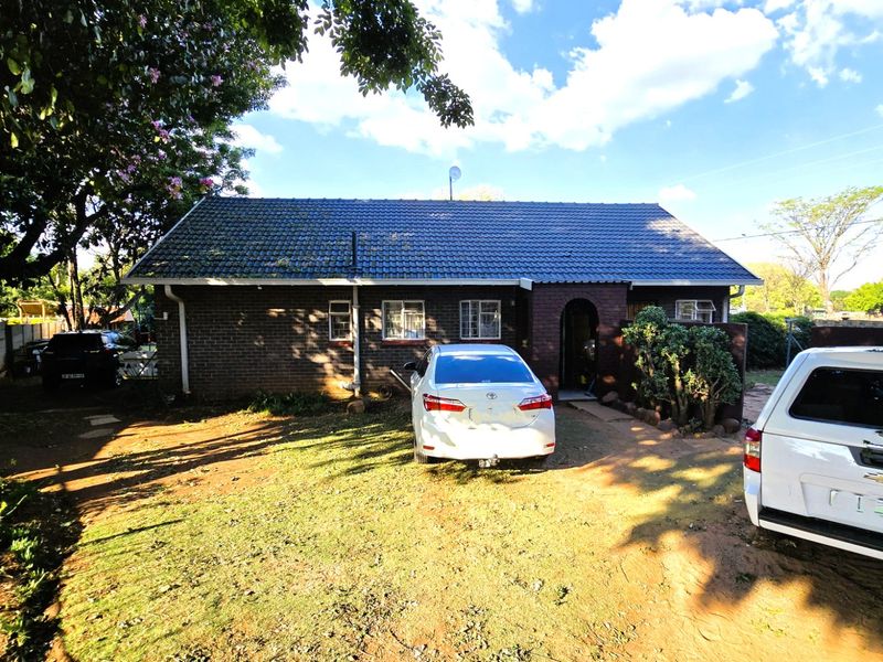 Front view of a single-story brick house featuring a tiled roof, arched entrance, and a spacious front yard with driveway access.