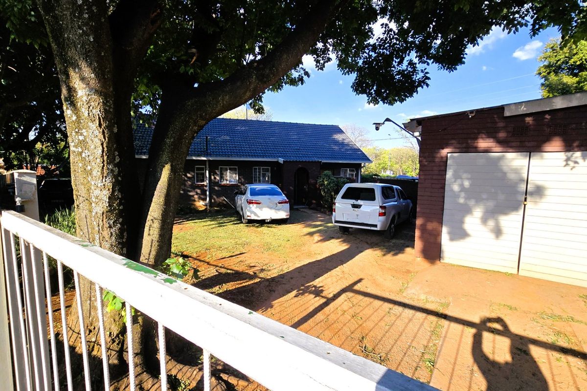 Front view of the property featuring a brick facade, tiled roof, and a detached garage with a paved driveway area.
