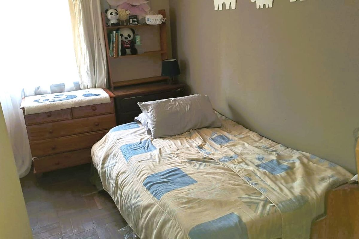 A compact bedroom featuring parquet flooring and natural light from a window with curtain rails.