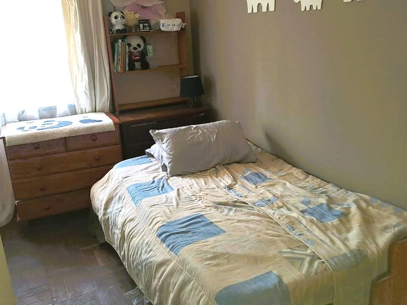 A compact bedroom featuring parquet flooring and natural light from a window with curtain rails.