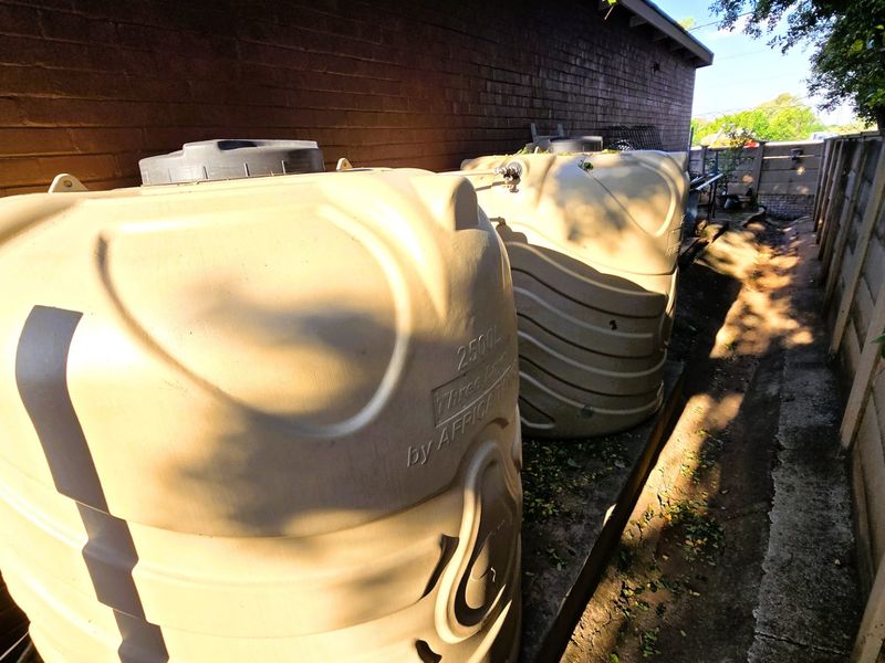 Side yard area featuring two large plastic water storage tanks installed against the exterior brick wall of the property.
