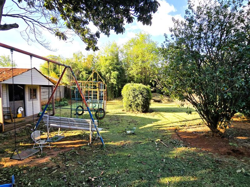 A spacious backyard featuring a detached outbuilding, mature trees, and an expansive lawn area.