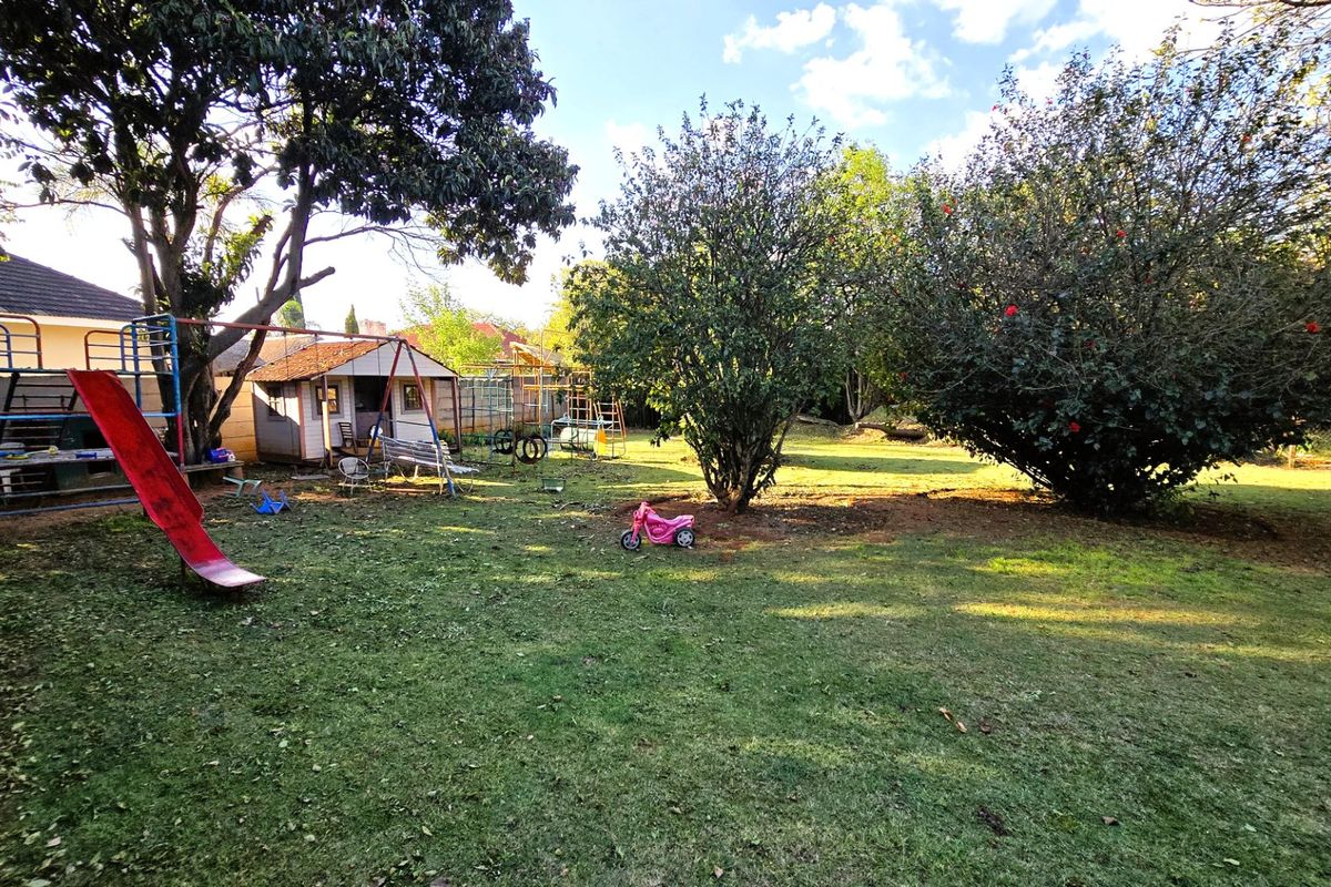 A spacious backyard featuring a large lawn, mature trees, and a detached outbuilding structure.