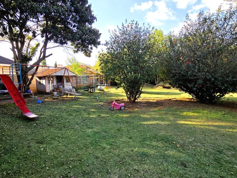 A spacious backyard featuring a large lawn, mature trees, and a detached outbuilding structure.