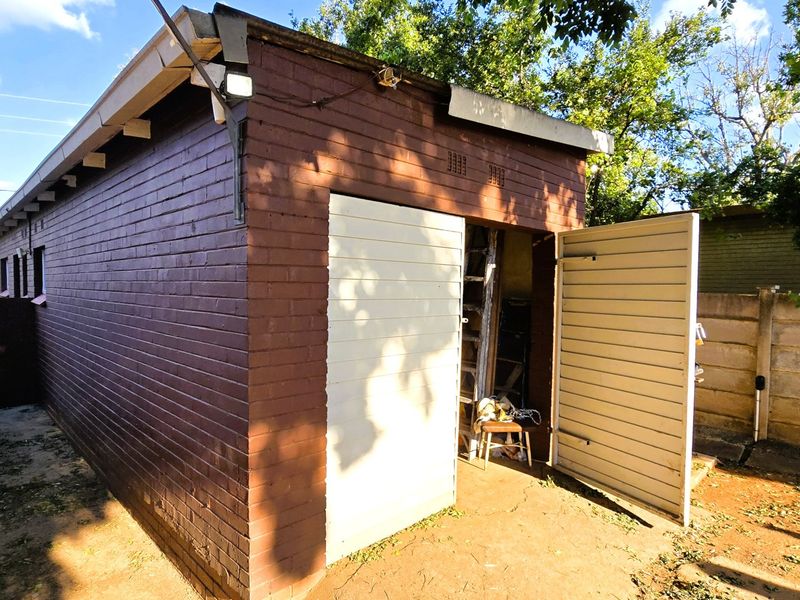 A detached brick garage featuring a hinged door and exposed rafter tails, situated in a residential yard setting.