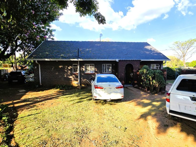 Front view of a single-story brick house with a tiled roof and an arched entrance, featuring a driveway and surrounding garden area.