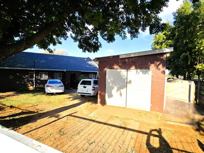 Front view of the property featuring a brick house with a tiled roof, a detached garage, and a spacious driveway area.