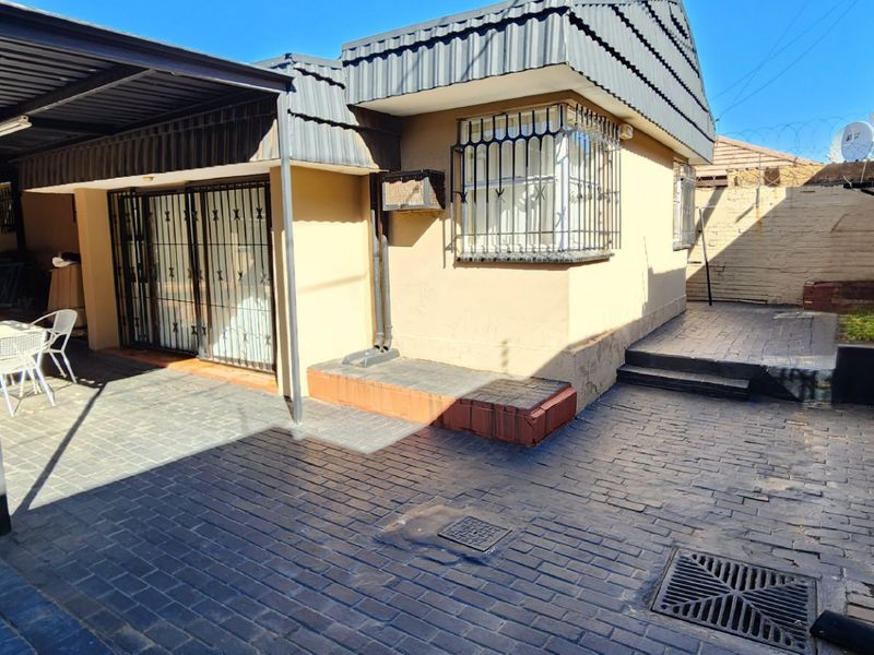 Rear exterior view featuring a paved courtyard, covered patio area, and secure window bars on the building facade.