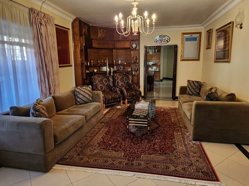 A spacious living room featuring tiled flooring, decorative cove cornicing, a central chandelier, and a built-in wooden display shelving unit.