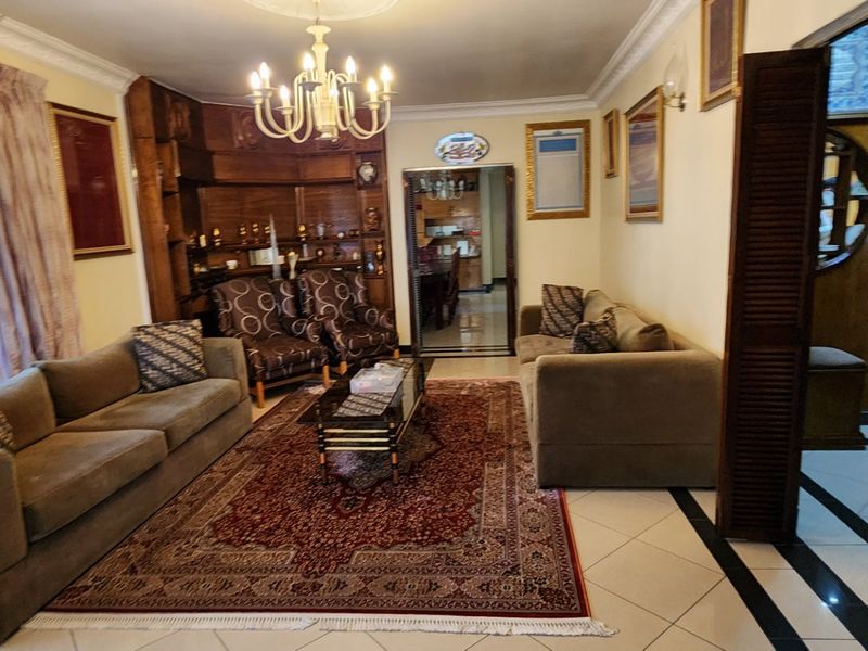A traditional living room featuring built-in wooden cabinetry, decorative ceiling cornices, a central chandelier, and tiled flooring with a classic layout.