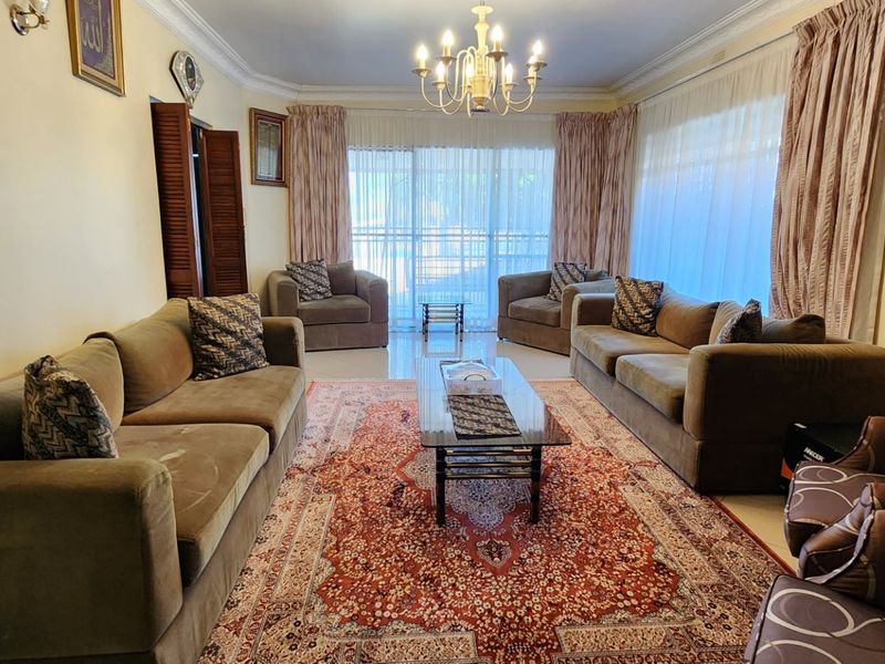A spacious living room featuring tiled flooring, decorative ceiling cornices, a central chandelier, and large sliding glass doors providing natural light.