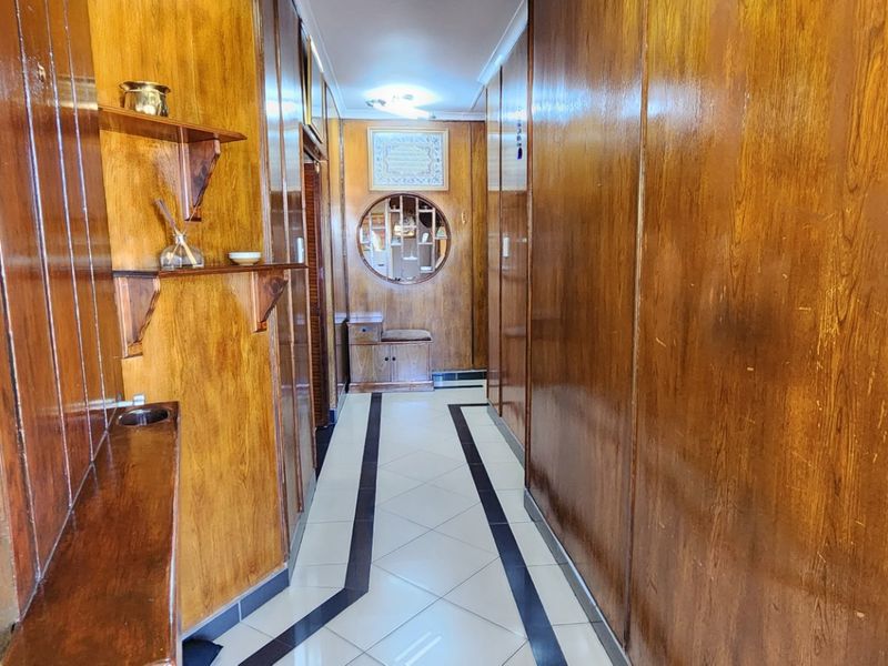 A long hallway featuring extensive wood wall paneling, tiled flooring with a decorative border, and a unique circular feature window.