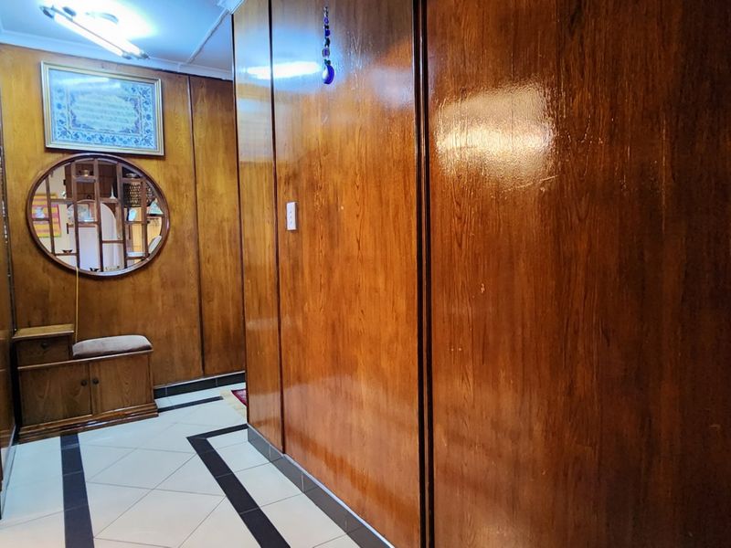 A hallway featuring extensive built-in wooden cabinetry, tiled flooring with decorative borders, and a louvered door.