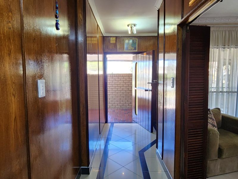 A hallway featuring wood-paneled walls and tiled flooring, leading towards an exterior entrance.