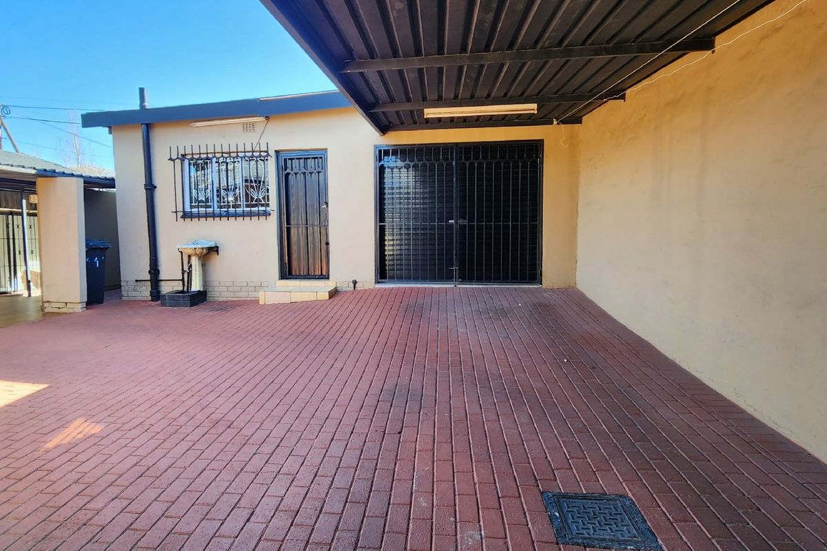 A paved rear courtyard area featuring a covered carport, security gates, and an external wash basin, providing functional outdoor space.