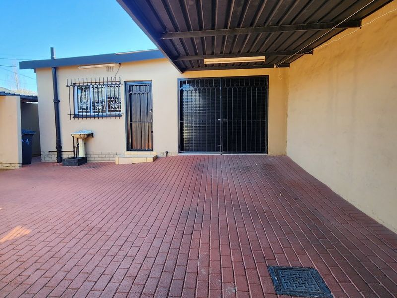 A paved rear courtyard area featuring a covered carport, security gates, and an external wash basin, providing functional outdoor space.