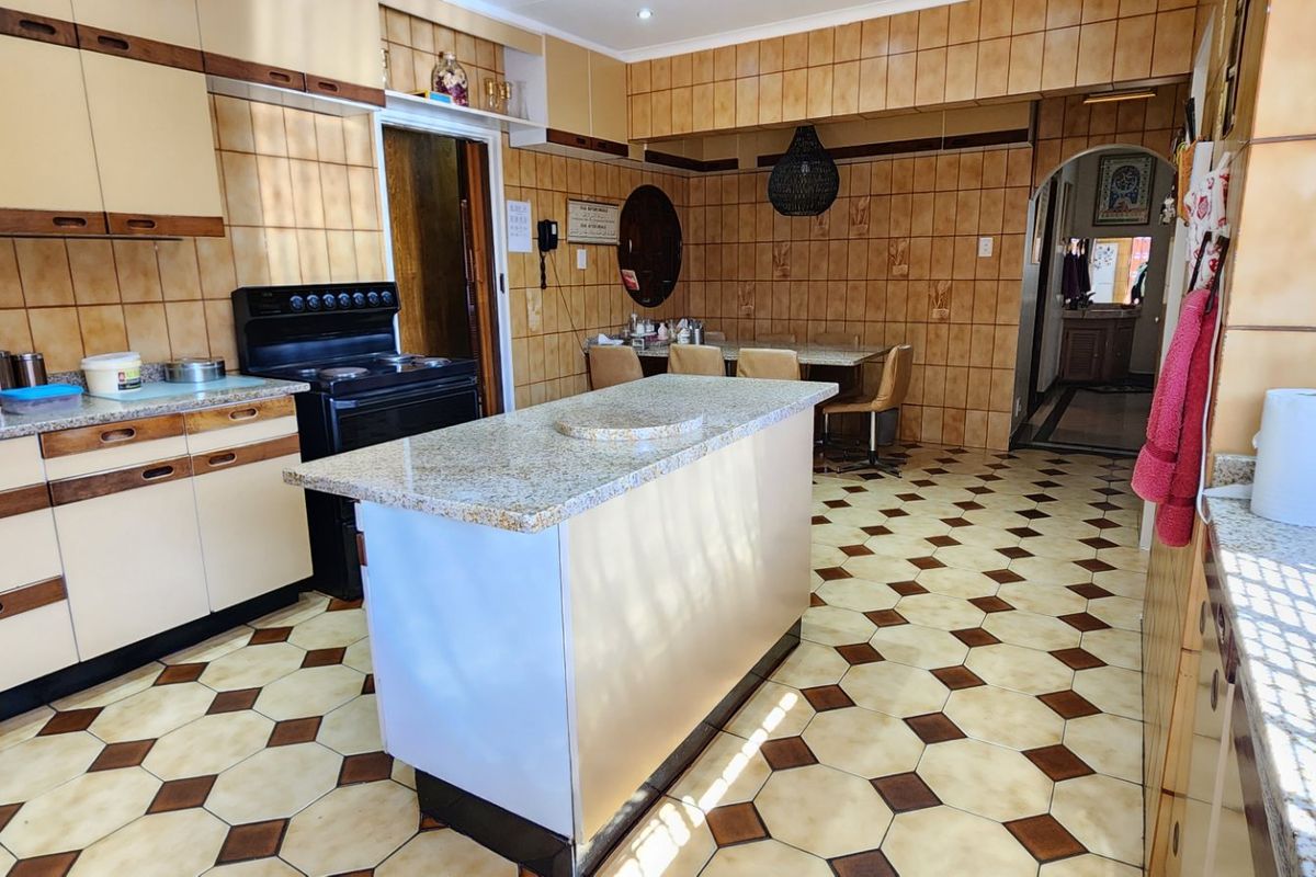 A spacious kitchen featuring granite countertops, a central island, and extensive wall tiling, offering a functional layout with potential for modern cosmetic updates.