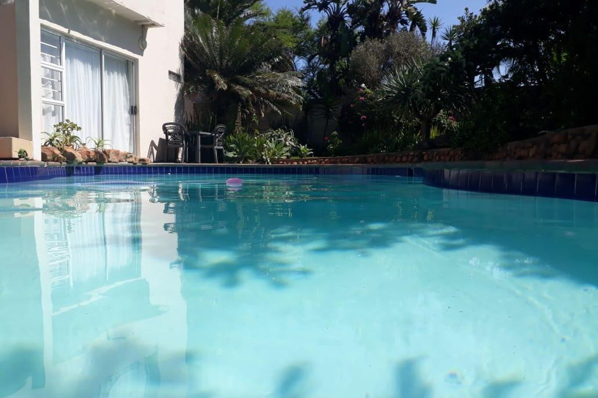 A well-maintained swimming pool area featuring tiled coping, adjacent to a private garden and direct access to the apartment via sliding glass doors.