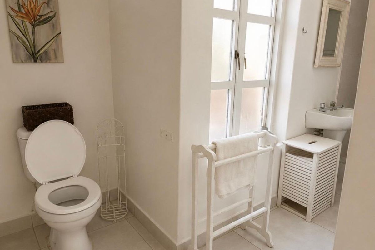 A functional bathroom featuring a pedestal basin, toilet, and tiled flooring, with natural light provided by a casement window and transom window.
