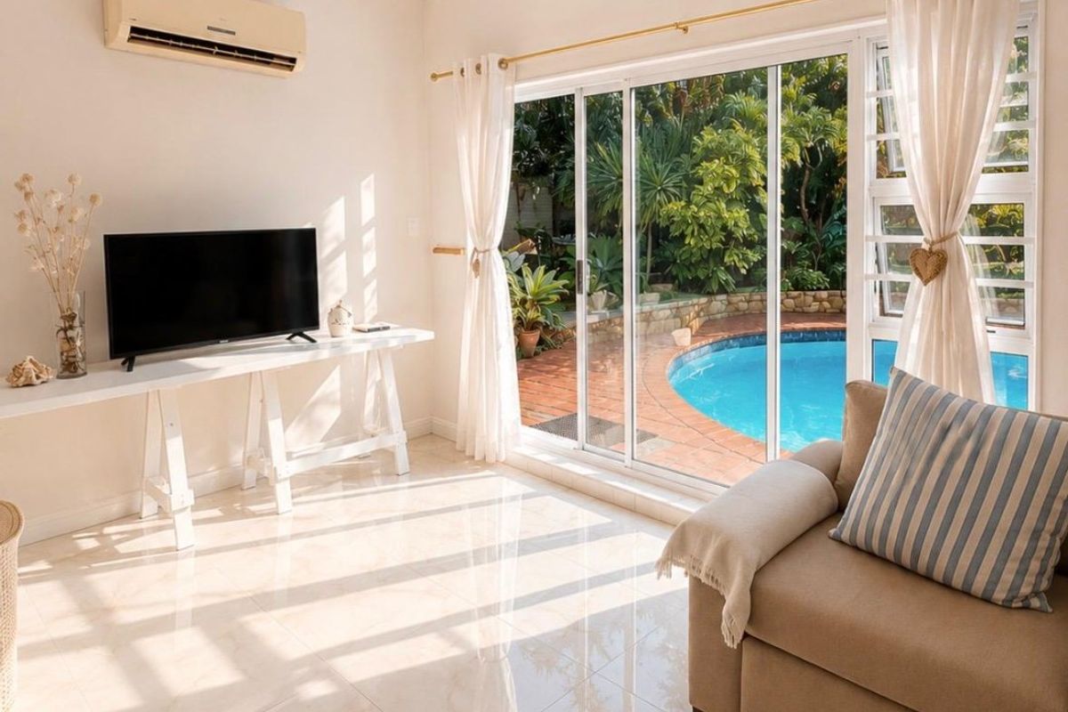 Bright living room featuring polished tiled floors, a wall-mounted air conditioner, and large sliding glass doors providing direct access to the pool area.