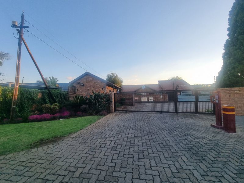 Front entrance view of the townhouse complex featuring a paved driveway, secure sliding gate, and well-maintained garden area.