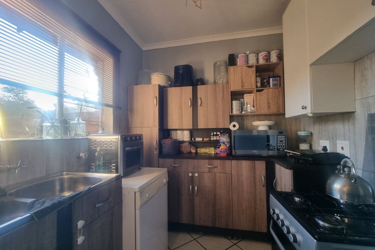 A functional kitchen featuring wood-look cabinetry, laminate countertops, a gas stove, and tiled flooring, offering a practical layout for daily meal preparation.