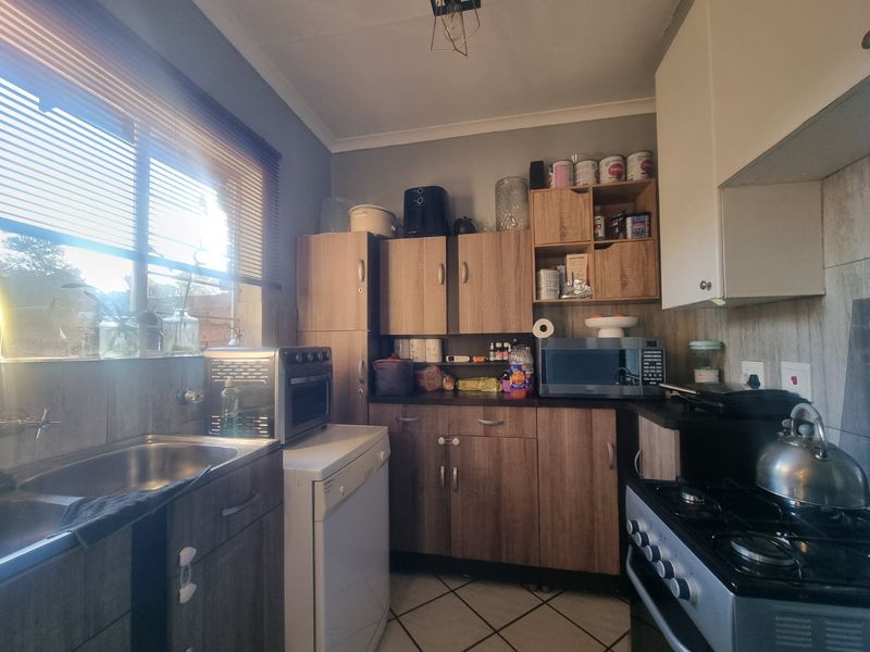 A functional kitchen featuring wood-look cabinetry, laminate countertops, a gas stove, and tiled flooring, offering a practical layout for daily meal preparation.