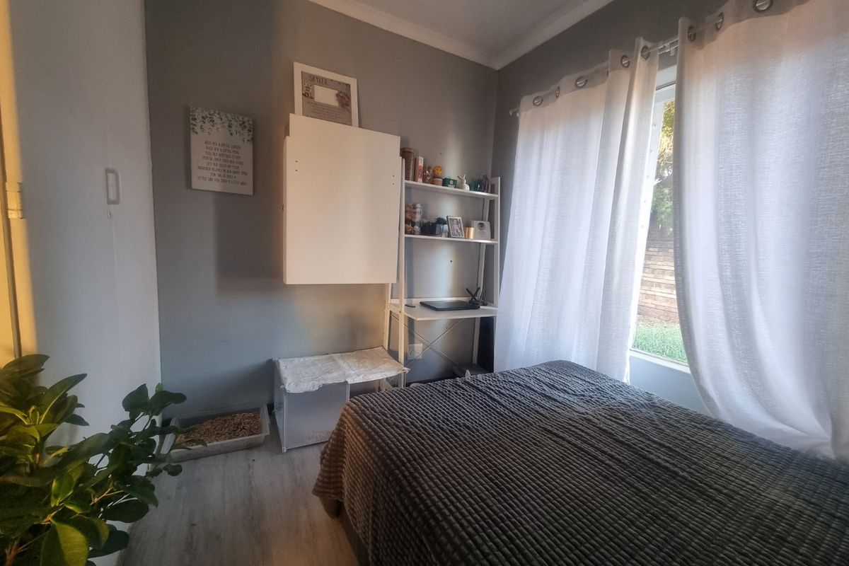 A cozy bedroom featuring light-toned laminate flooring and natural light through a window with installed curtain tracks.