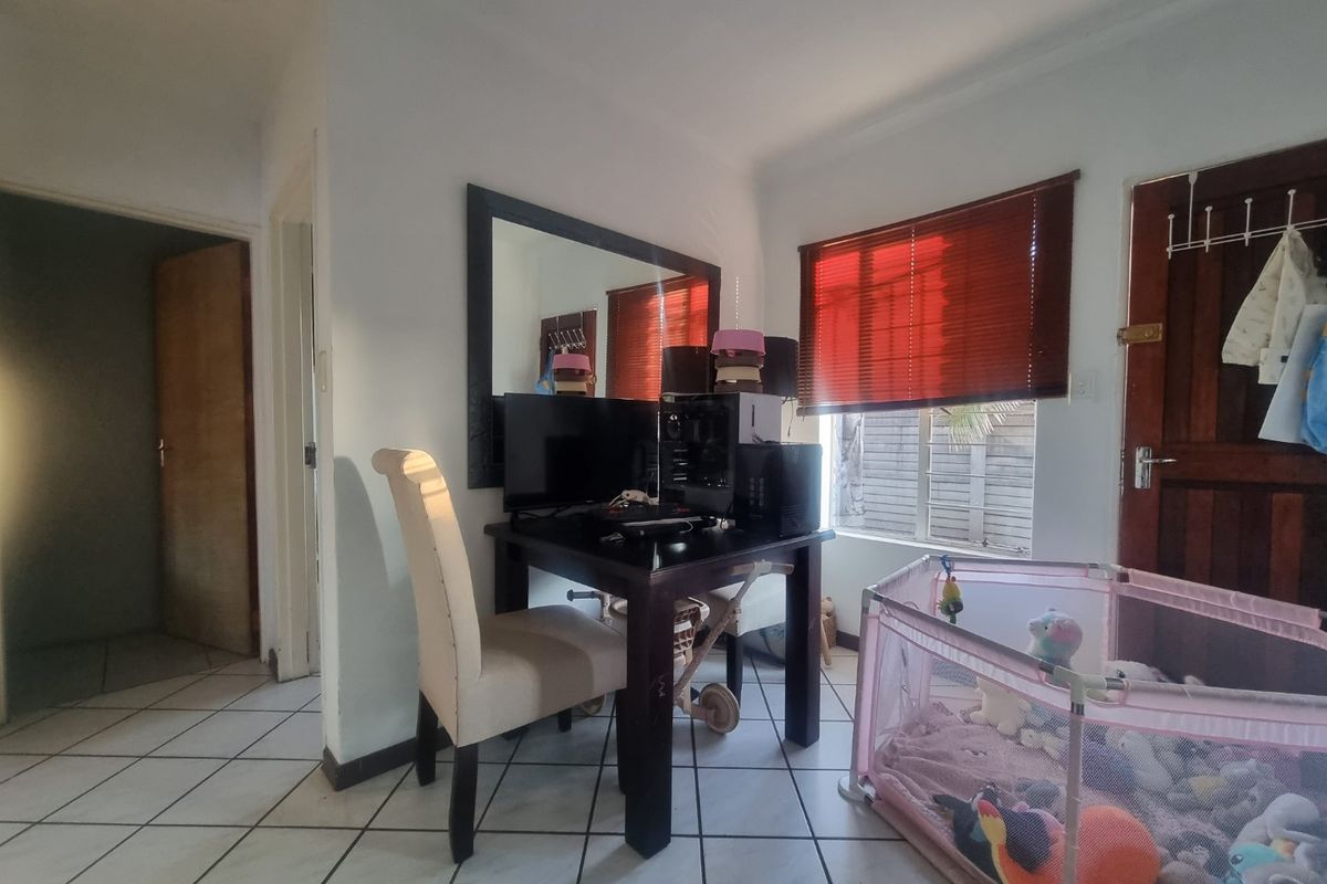 A living area featuring tiled flooring, timber door, and venetian blinds, currently utilized as a multi-purpose space.
