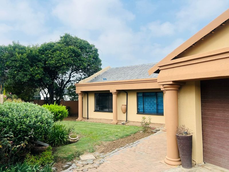 Front view of a single-story house featuring a paved driveway, concrete columns, and a well-maintained garden area.