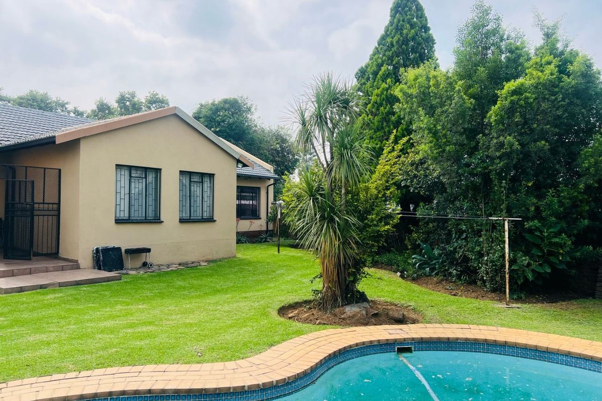 Rear view of the property featuring a well-maintained lawn, a swimming pool with tiled coping, and security bars on the windows.